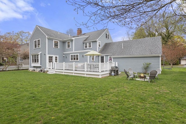 rear view of house featuring a chimney, a yard, a fire pit, a wooden deck, and roof with shingles