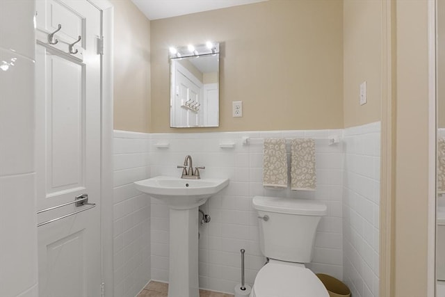bathroom featuring toilet, tile walls, a sink, and wainscoting