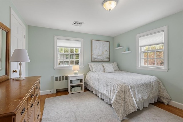 bedroom with multiple windows, visible vents, wood finished floors, and radiator