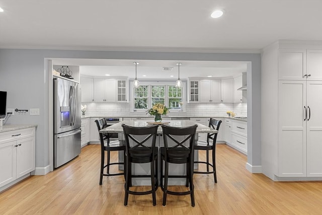 kitchen with stainless steel fridge, white cabinets, a breakfast bar, and light wood-style floors