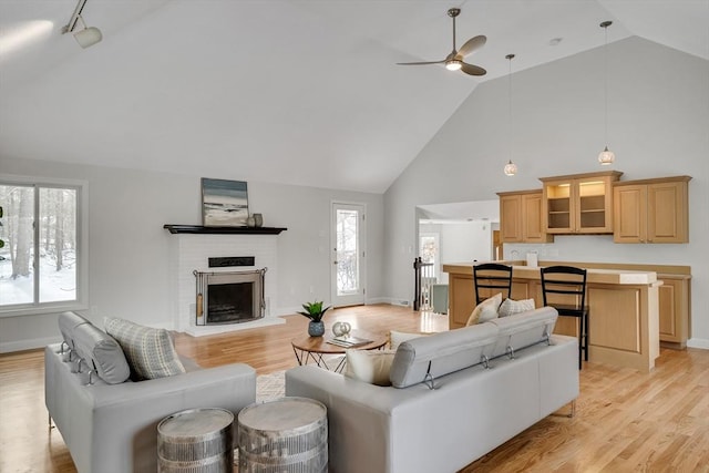 living room with a brick fireplace, high vaulted ceiling, ceiling fan, and light wood-type flooring