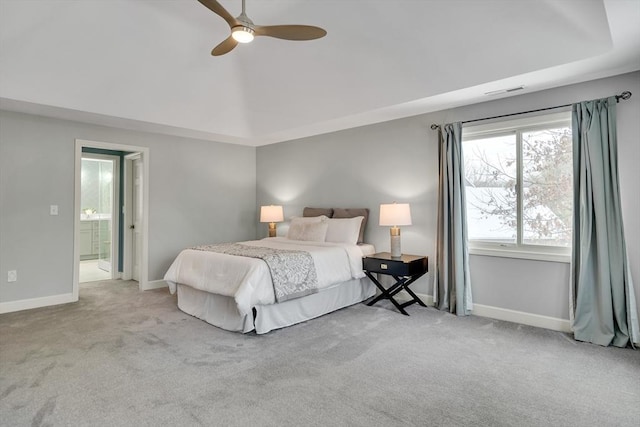 carpeted bedroom with ceiling fan, a raised ceiling, and ensuite bath