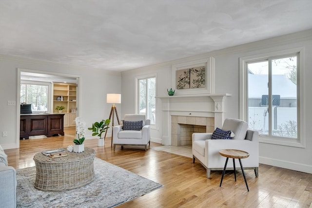 living area with a tiled fireplace, built in shelves, a wealth of natural light, and light hardwood / wood-style flooring