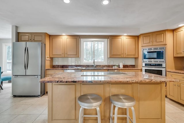 kitchen featuring a breakfast bar, sink, appliances with stainless steel finishes, a kitchen island, and light stone countertops