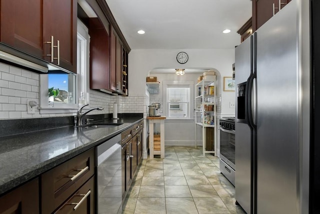 kitchen featuring dark stone countertops, appliances with stainless steel finishes, sink, backsplash, and light tile patterned floors