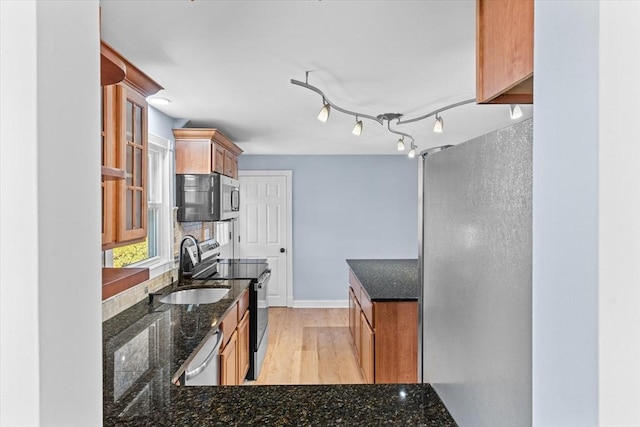 kitchen with a sink, baseboards, appliances with stainless steel finishes, light wood finished floors, and dark stone countertops