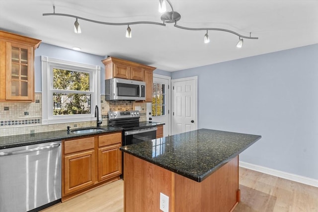 kitchen with brown cabinets, light wood-style flooring, decorative backsplash, appliances with stainless steel finishes, and a sink