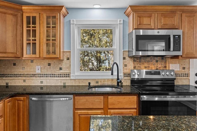 kitchen featuring stainless steel appliances, brown cabinetry, a sink, and dark stone countertops