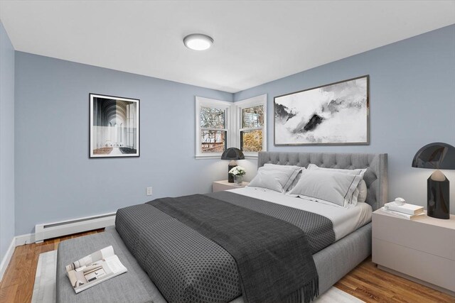 bedroom with a baseboard heating unit, wood finished floors, and baseboards