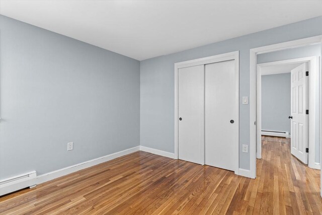 unfurnished bedroom featuring a baseboard radiator, baseboards, light wood-style floors, baseboard heating, and a closet