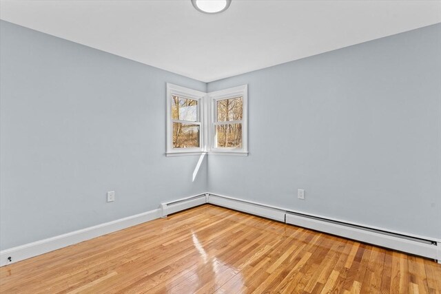 empty room with light wood-type flooring, a baseboard radiator, and baseboards