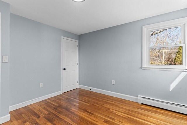 spare room with baseboards, a baseboard heating unit, and wood finished floors