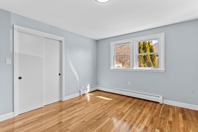 unfurnished bedroom featuring light wood-type flooring, a closet, baseboards, and baseboard heating