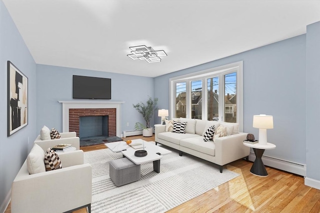 living room featuring baseboard heating, a fireplace, light wood-style flooring, and baseboards