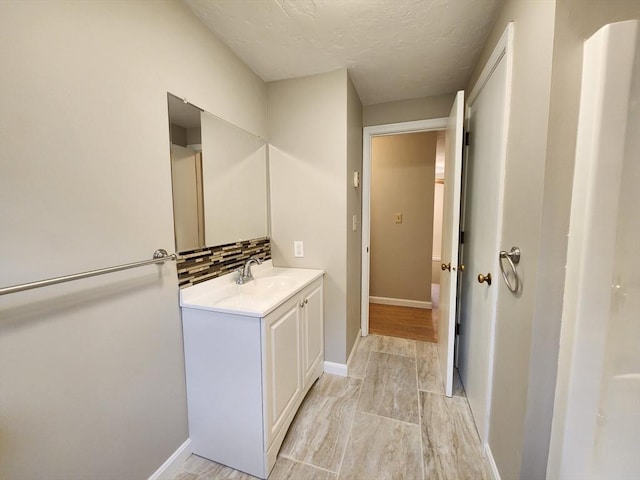 bathroom with baseboards, decorative backsplash, wood finished floors, a textured ceiling, and vanity