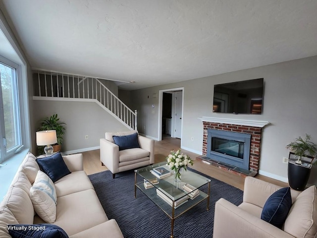 living area featuring stairway, a fireplace, wood finished floors, and baseboards