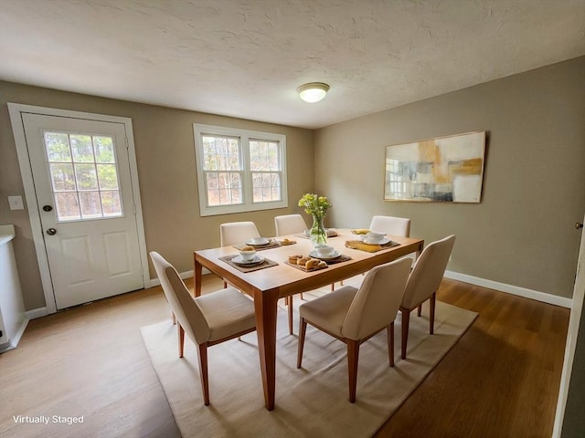 dining area featuring a textured ceiling, light wood-style flooring, a wealth of natural light, and baseboards