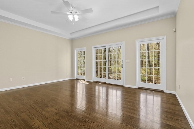 unfurnished room with baseboards, ceiling fan, a tray ceiling, and dark wood-style floors