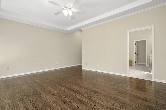 empty room with a raised ceiling, a ceiling fan, baseboards, dark wood-type flooring, and ornamental molding