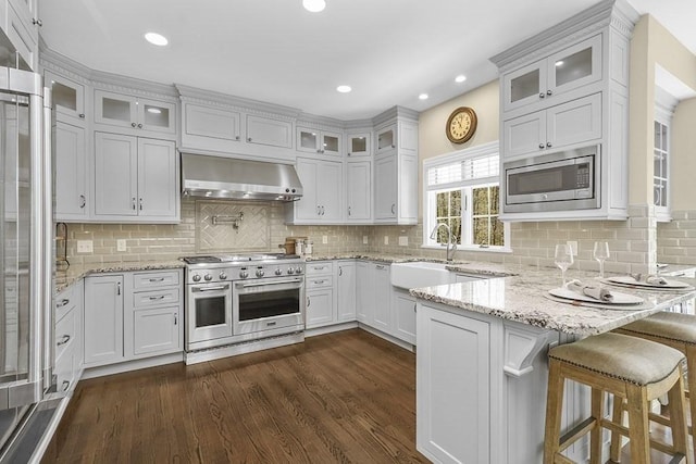kitchen featuring wall chimney range hood, a sink, a peninsula, dark wood-style floors, and premium appliances