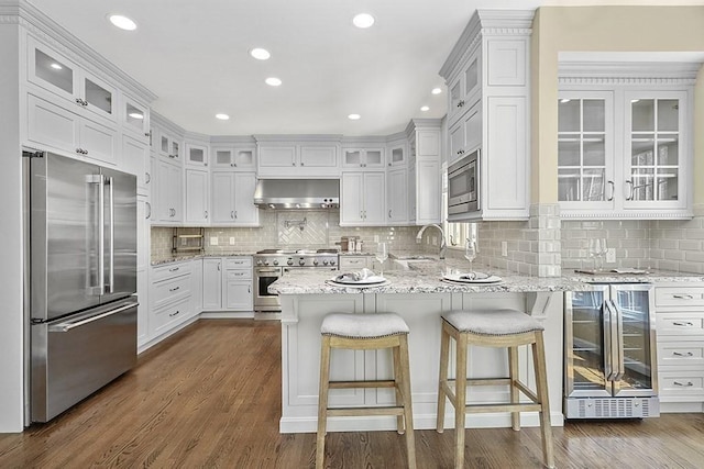 kitchen with extractor fan, a peninsula, high end appliances, decorative backsplash, and wine cooler