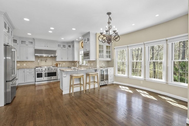 kitchen with an inviting chandelier, a peninsula, wall chimney exhaust hood, a sink, and appliances with stainless steel finishes