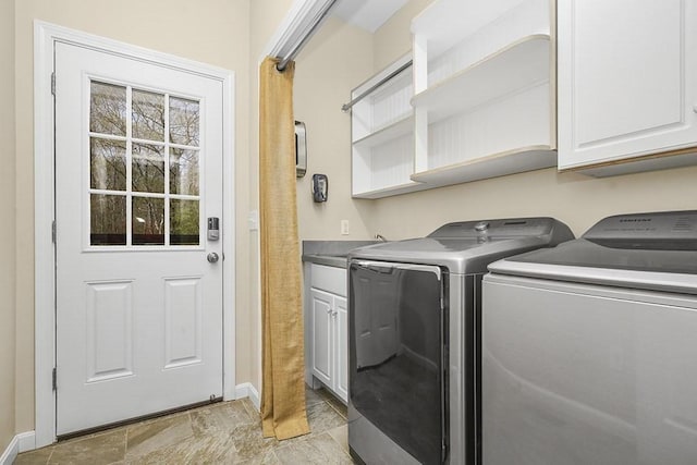 clothes washing area featuring cabinet space, baseboards, stone finish floor, and washer and clothes dryer