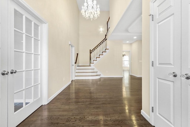 foyer entrance featuring a notable chandelier, stairs, baseboards, a towering ceiling, and dark wood-style floors