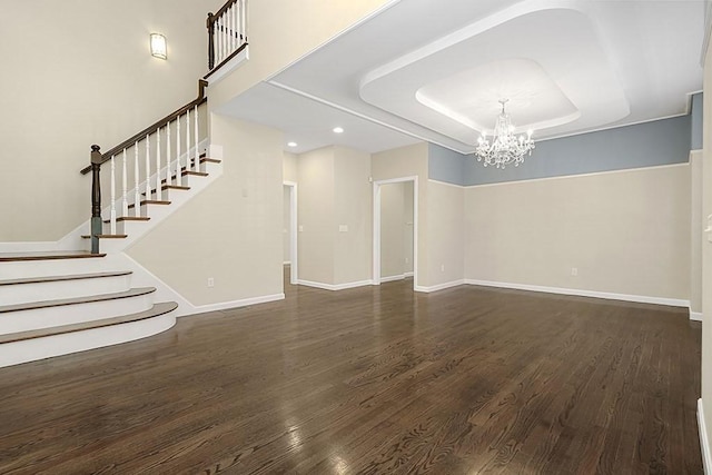 unfurnished living room with stairway, a tray ceiling, wood finished floors, and a chandelier