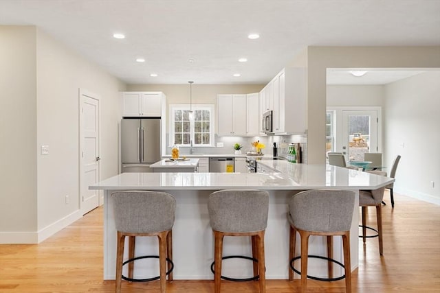 kitchen with white cabinets, stainless steel appliances, a kitchen breakfast bar, hanging light fixtures, and kitchen peninsula