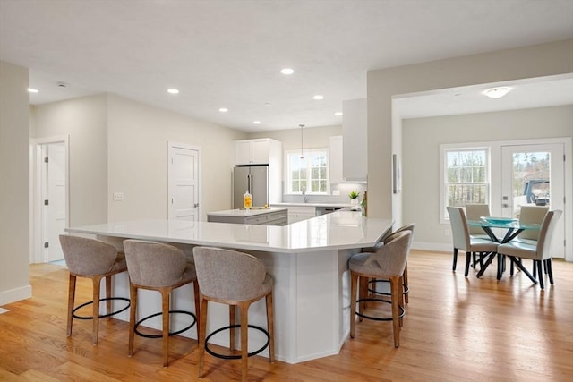 kitchen with white cabinets, decorative light fixtures, light hardwood / wood-style floors, stainless steel fridge, and kitchen peninsula