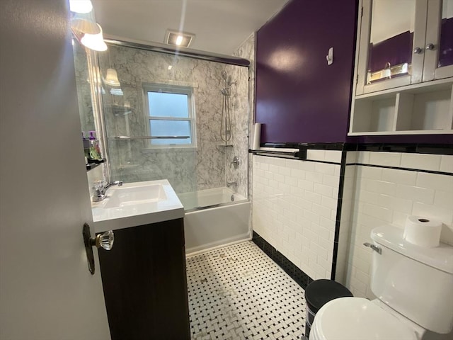 full bathroom featuring vanity, toilet, combined bath / shower with glass door, and tile walls