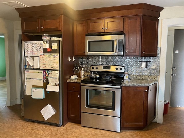 kitchen featuring backsplash, light hardwood / wood-style flooring, light stone countertops, and appliances with stainless steel finishes