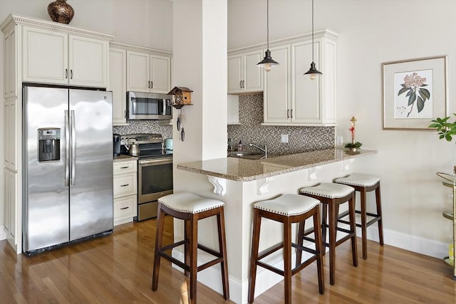 kitchen featuring white cabinetry, hanging light fixtures, kitchen peninsula, a breakfast bar area, and appliances with stainless steel finishes