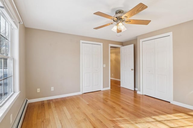 unfurnished bedroom featuring baseboard heating, two closets, light hardwood / wood-style floors, and ceiling fan