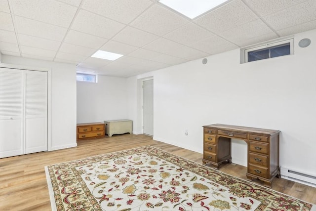 interior space with wood-type flooring, a drop ceiling, and a baseboard radiator