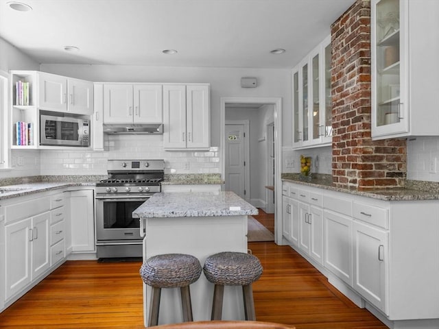 kitchen with dark wood-style floors, under cabinet range hood, white cabinets, appliances with stainless steel finishes, and backsplash