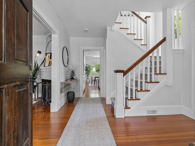 foyer with stairway, baseboards, wood finished floors, and visible vents