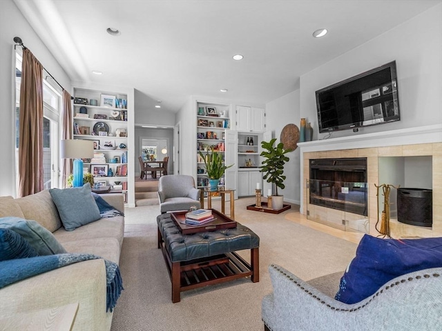 living area with recessed lighting, a tiled fireplace, and built in shelves