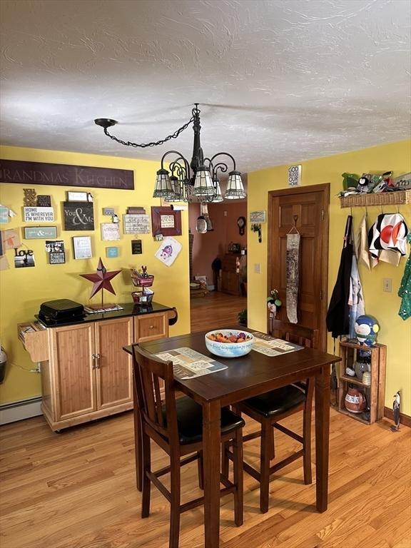 37 Teaberry Ln, Gardner, MA 01440 - dining area featuring light wood-style floors, a chandelier, a textured ceiling, and a baseboard heating unit