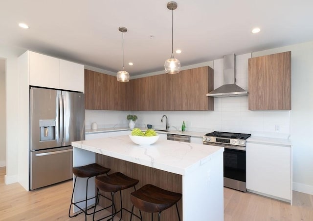 kitchen with a breakfast bar, light wood-style flooring, appliances with stainless steel finishes, a kitchen island, and wall chimney range hood