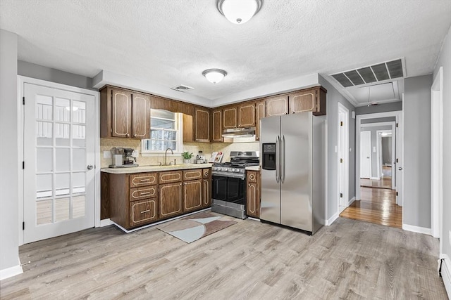 kitchen featuring under cabinet range hood, stainless steel appliances, visible vents, light countertops, and light wood finished floors