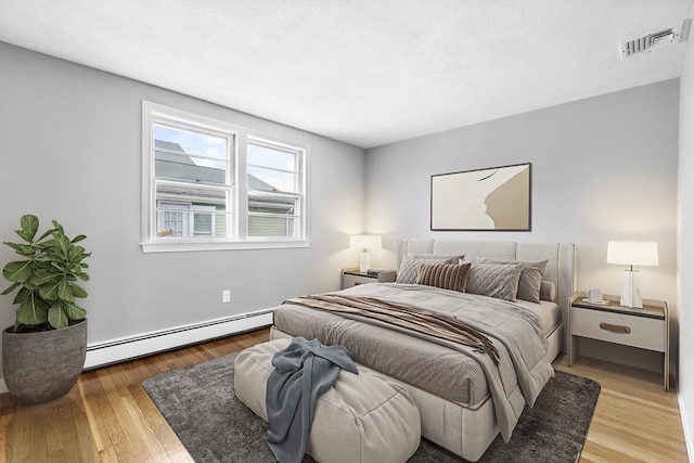 bedroom featuring visible vents, baseboard heating, and wood finished floors