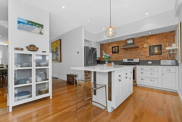 kitchen featuring appliances with stainless steel finishes, wall chimney exhaust hood, white cabinets, pendant lighting, and a kitchen island