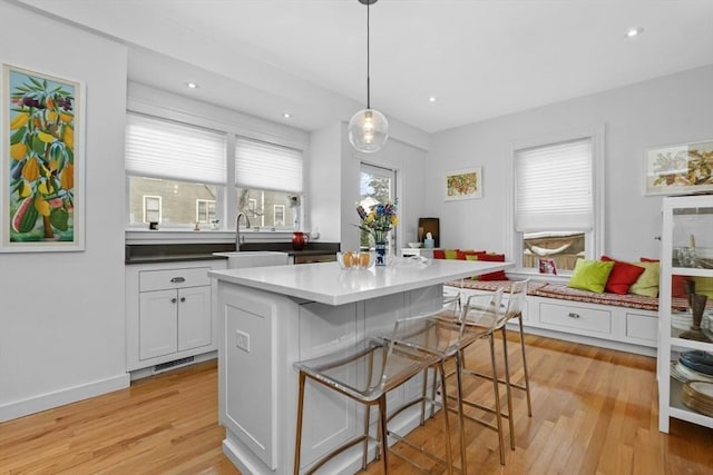 kitchen featuring white cabinets, decorative light fixtures, a center island, sink, and a kitchen bar