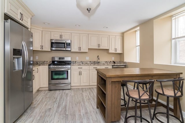 kitchen featuring light stone counters, appliances with stainless steel finishes, cream cabinetry, and light hardwood / wood-style flooring