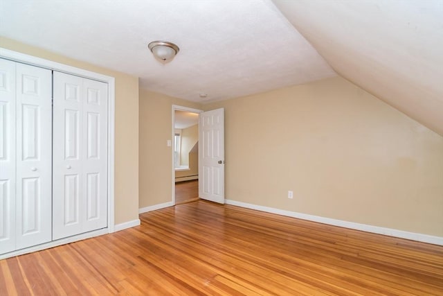 unfurnished bedroom with wood-type flooring, a baseboard radiator, a closet, and vaulted ceiling