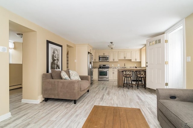 living room with baseboard heating, light hardwood / wood-style floors, and sink