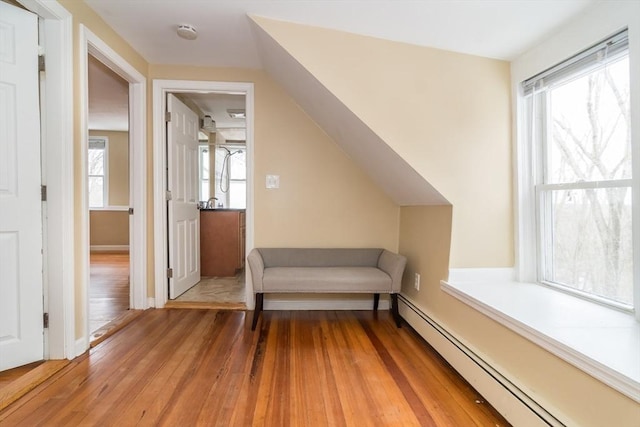 living area featuring baseboard heating, hardwood / wood-style floors, and vaulted ceiling