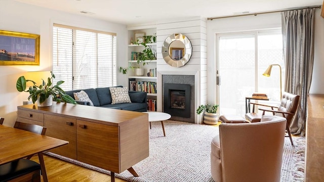 living room with a glass covered fireplace, plenty of natural light, visible vents, and light wood finished floors